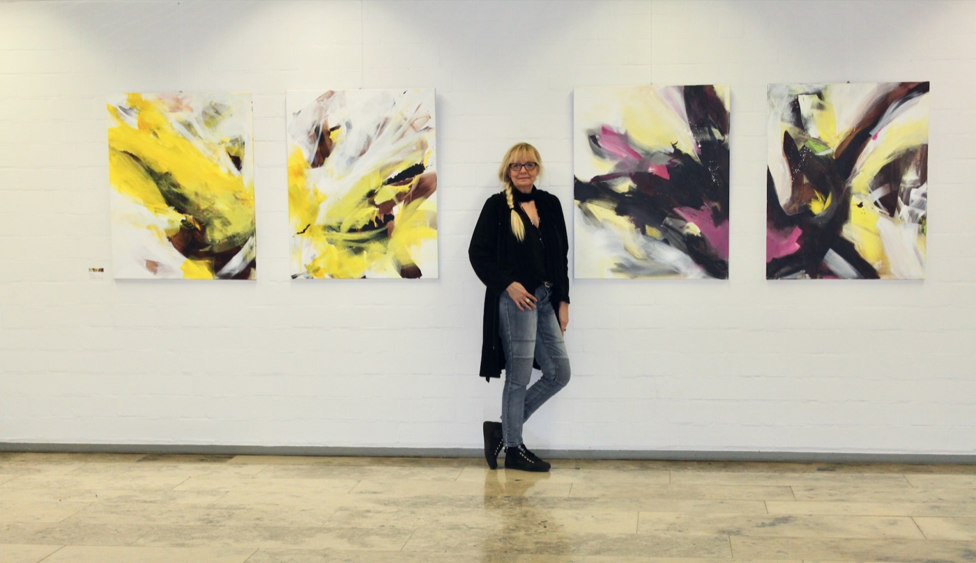 Silvia Grasser vor vier ihrer Bilder an einer langen weißen Wand