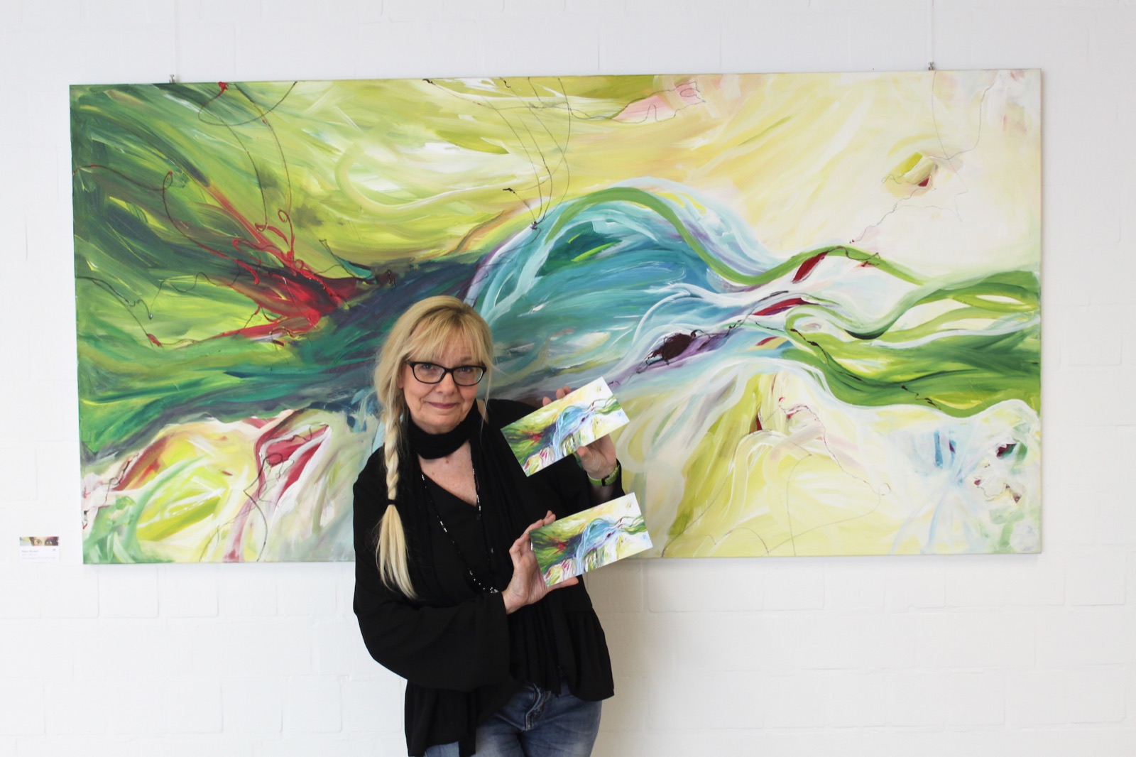 Silvia Grasser stützt lächelnd das Kinn in die Hand, hinter ihr ihr Acrylbild „Magic Moment“