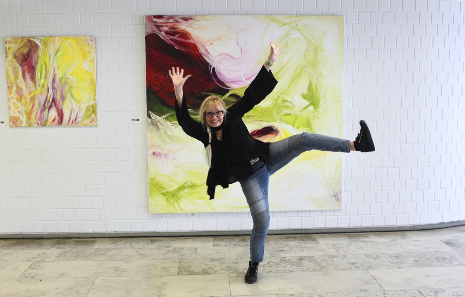Silvia Grasser springt fröhlich vor ihren Bildern – Malworkshops im Atelier