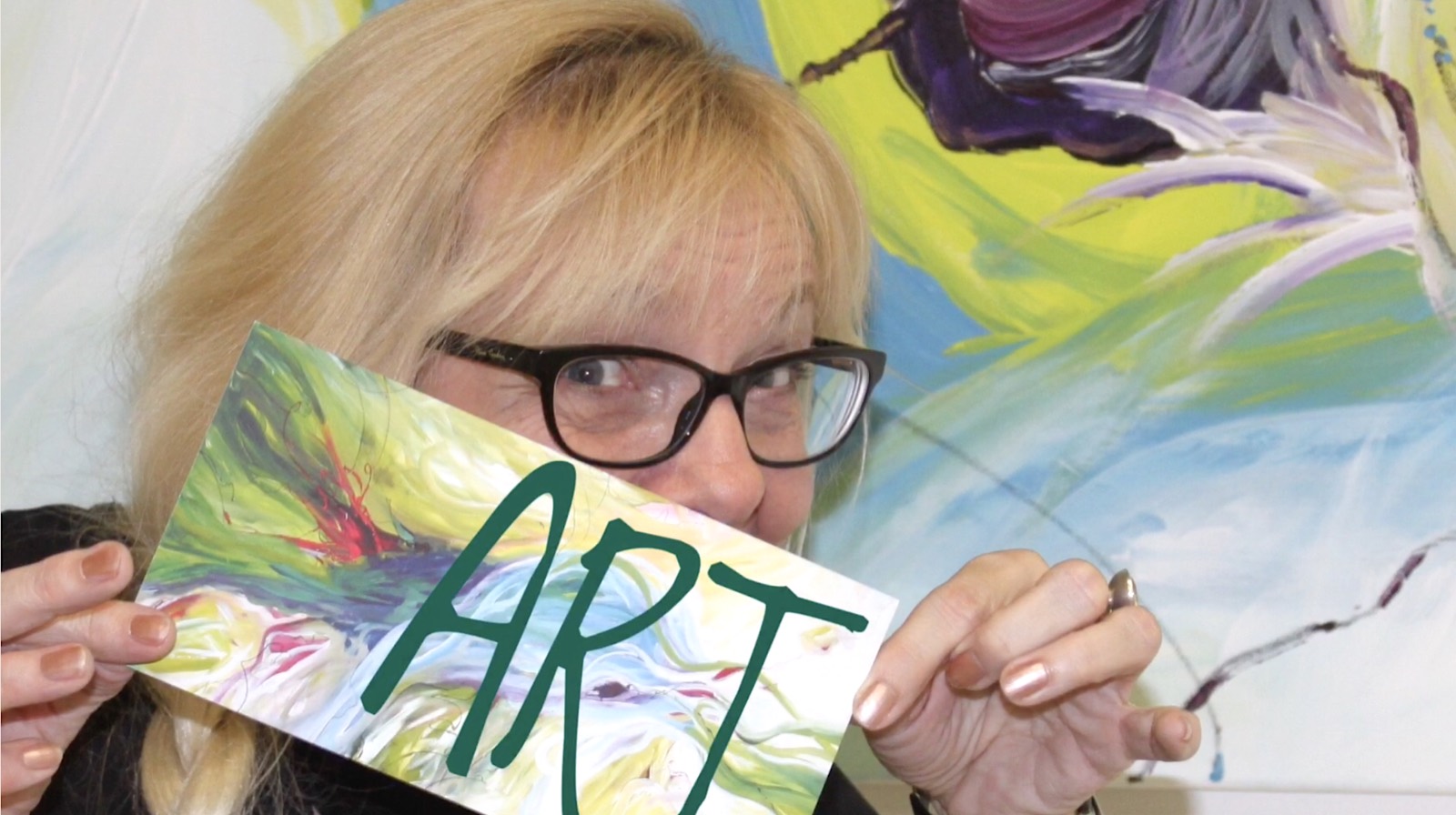 Silvia Grasser hält schmunzelnd eine bemalte Karte mit dem Schriftzug ART vor ihr Gesicht